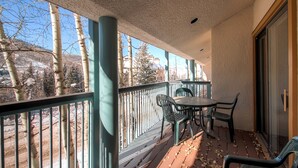 A balcony with a table and chairs, a railing, and a view of trees and buildings. - Centennial 2 Bedroom Condo Unit no. 7 (Avon)