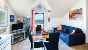 Una sala moderna con un sofá azul, un televisor, un aparador de vidrio y un comedor con mesa y sillas.