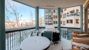 A balcony with a table and chairs, a stack of firewood, and a view of a multi-story building with balconies. - Centennial 2 Bedroom Condo Unit no. 3 (Avon)
