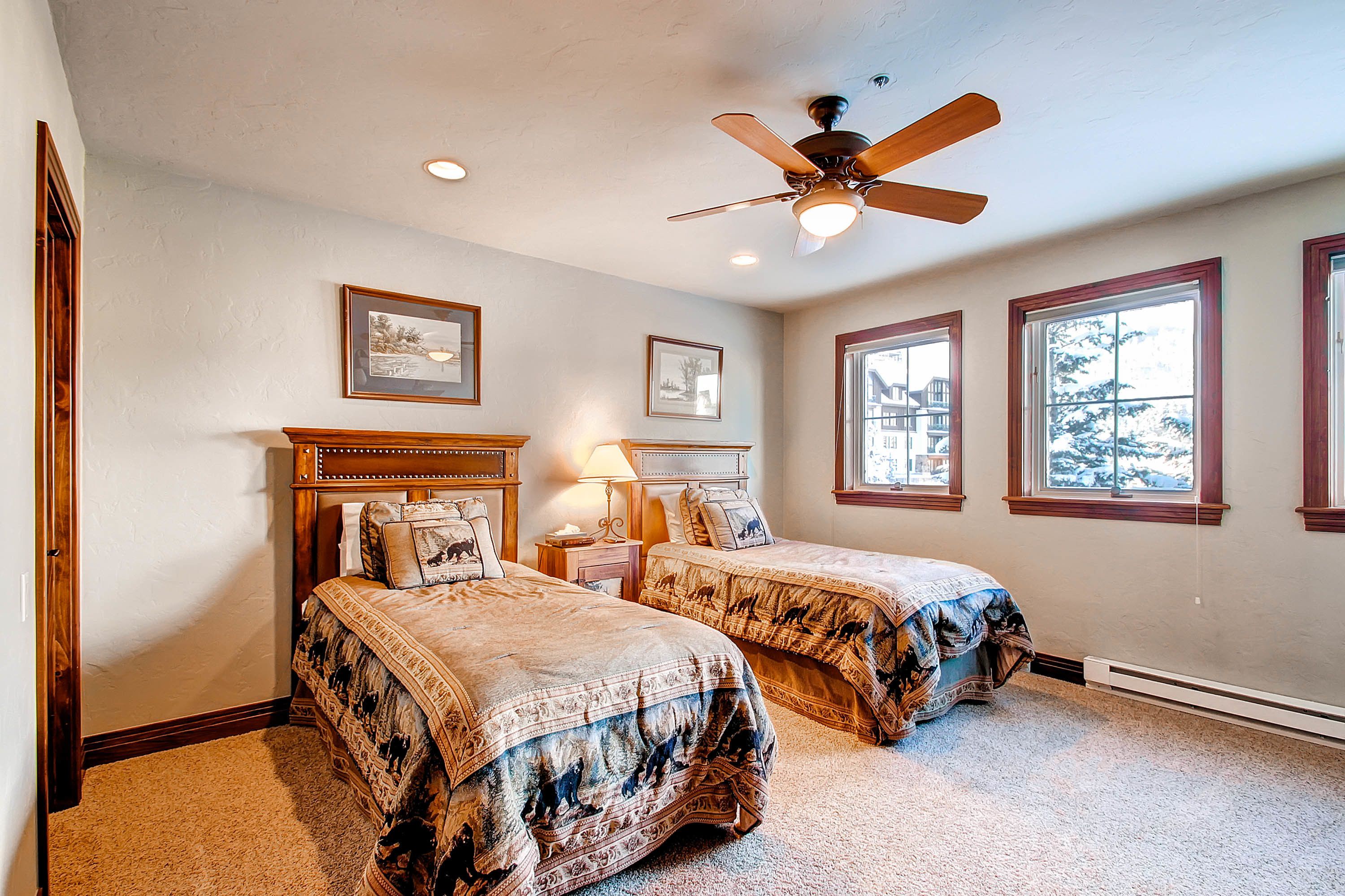 A bedroom with two beds, a ceiling fan, and large windows.