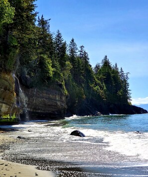 A rocky beach with a waterfall and dense forest.