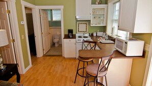 A compact kitchen with a central island, a microwave, and a stove. There is a door leading to a bathroom. - Lori Lanes 'romeo Cottage' ~ 2 Bedroom ~ Downtown (Ashland)