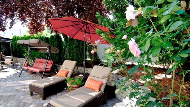 A patio area with two cushioned chairs and a swing chair, a red umbrella, and a climbing rose bush. - Lori Lanes 'romeo Cottage' ~ 2 Bedroom ~ Downtown (Ashland)
