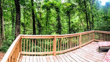 Relax on the deck with a view of the lush forest, surrounded by two comfortable chairs and a small table.