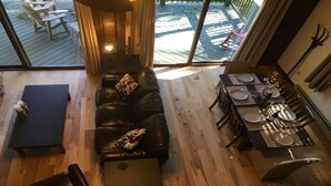 Ein modernes Wohnzimmer mit einer schwarzen Ledersofa, einem Esstisch für zwei Personen und Blick auf die Terrasse durch große Fenster.