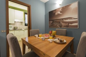 Ein Essbereich mit Holztisch, Stühlen, Frühstücksgebäck und einer Küche im Hintergrund.