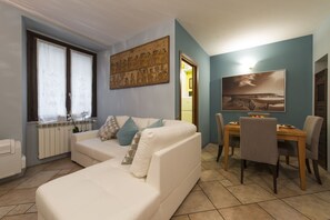 Ein Wohnzimmer mit weißem Sofa, einem Esstisch mit Stühlen, einem Heizkörper und einem Bild an der Wand.