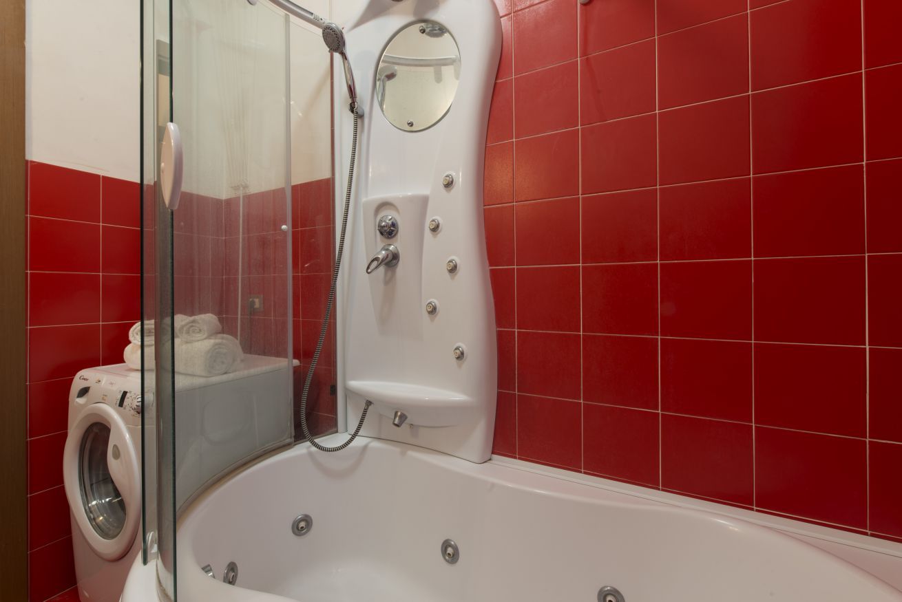 A bathroom with a glass-enclosed shower, a white bathtub, and a washing machine.