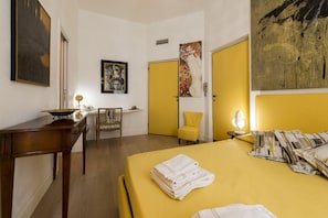 Une chambre d’hôtel avec un lit, un bureau, une chaise et des œuvres d’art accrochées aux murs.