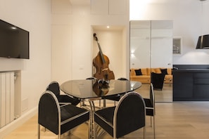 Un salon moderne avec une table à manger en verre, des chaises noires, un téléviseur fixé au mur et un tapis.