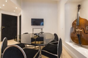 A modern room with a glass table surrounded by chairs, a television on the wall, and a cello on display.