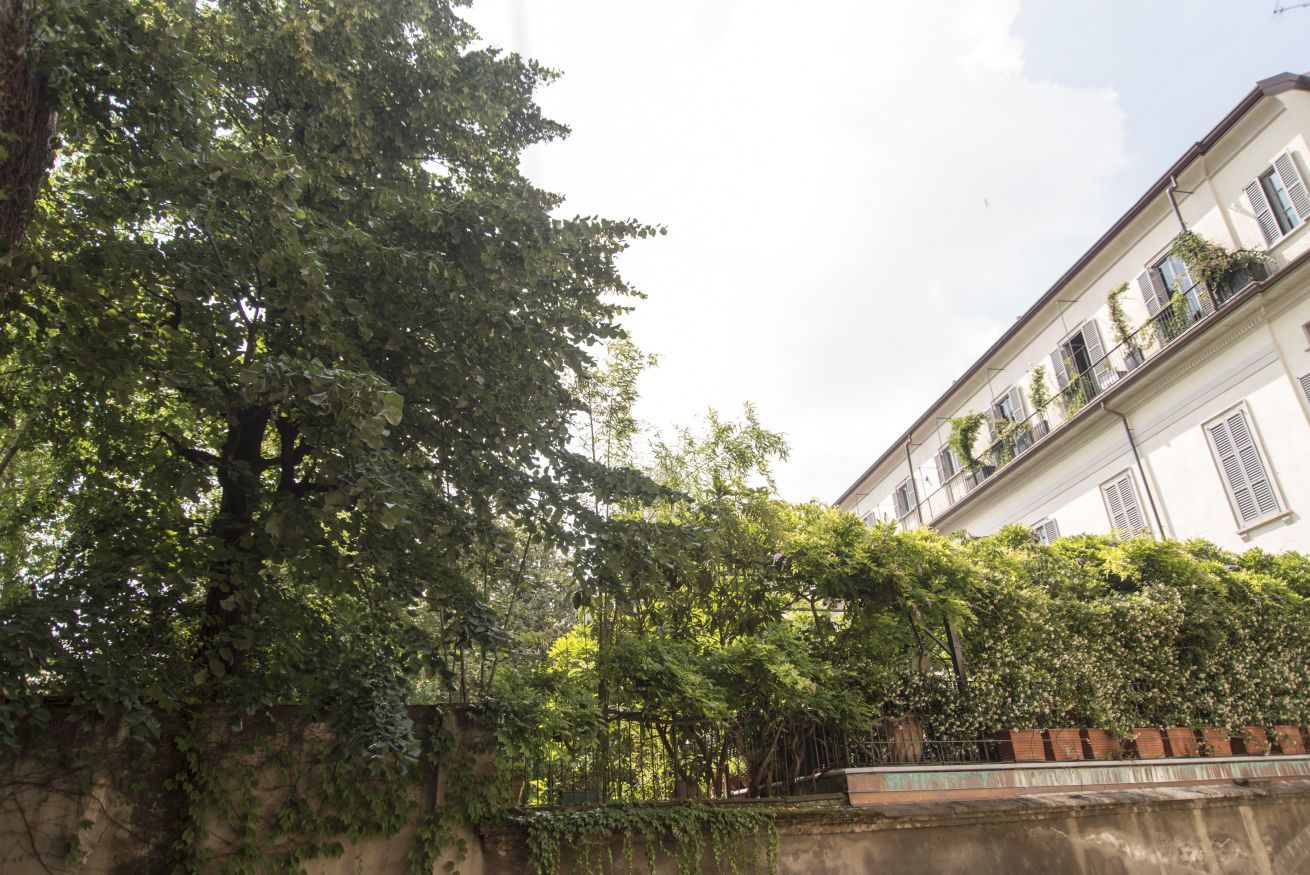 Um edifício com fachada branca, várias janelas e uma varanda com vegetação.