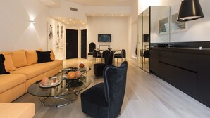 A modern living room with a sofa, a coffee table with decorative items, a dark chair, a dining area with chairs, and a kitchen with a large mirror and black cabinets. - Smart and design flat in Brera close to Alla Scala theatre (Milano)