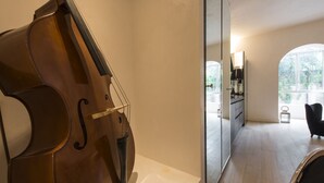 A room with a cello, a mirror, a black chair, and a view of a kitchen and dining area. - Smart and design flat in Brera close to Alla Scala theatre (Milano)