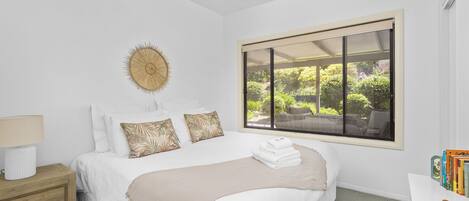 A bedroom with a bed, a nightstand, a window with a view of greenery, and a ceiling fan.
