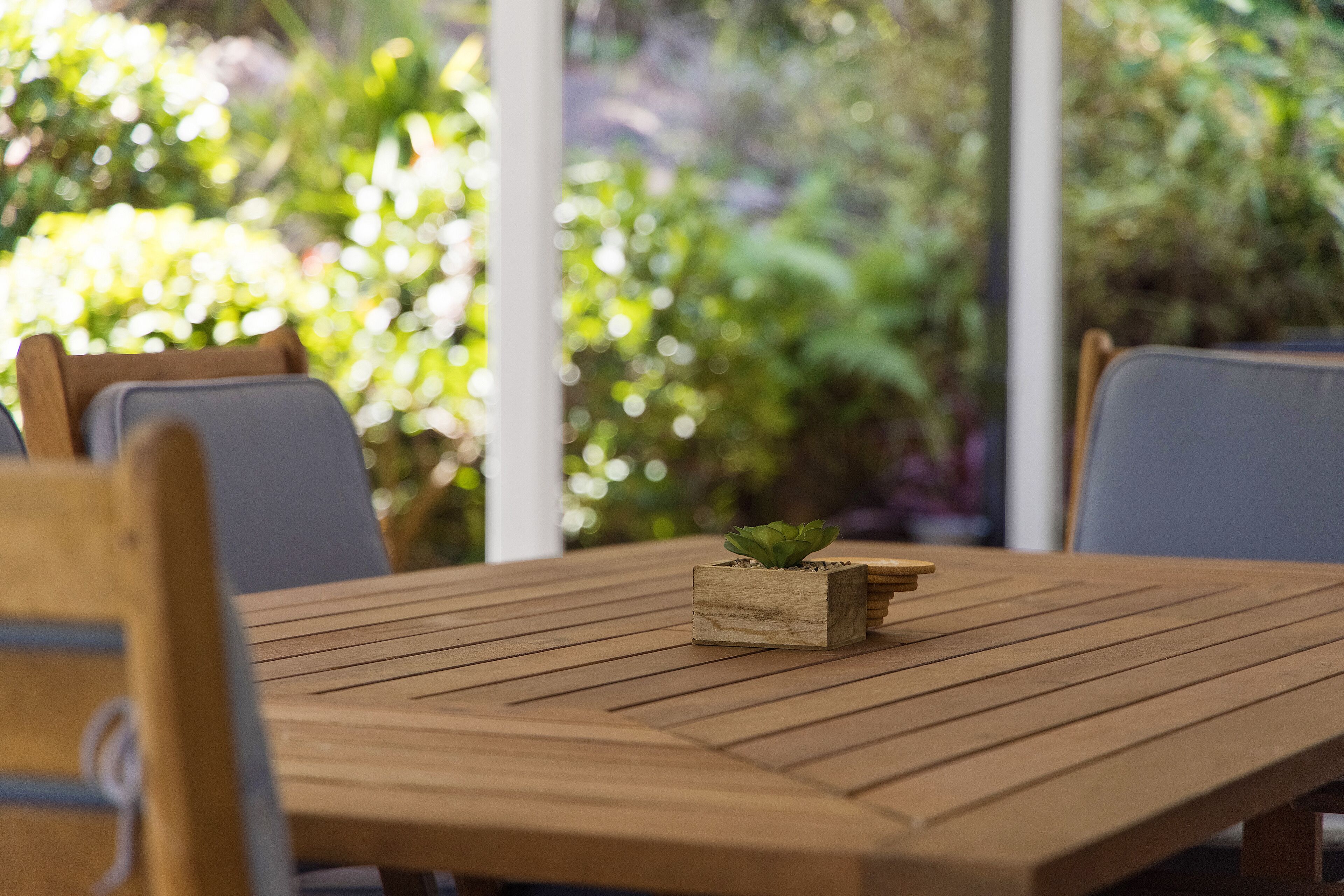 A wooden table with a small plant in a wooden planter, surrounded by chairs.