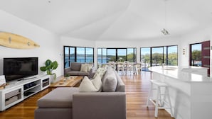 A spacious living area with a large flat-screen TV, a grey sofa, and a wooden coffee table. - Wanda Point House - pure tranquillity and walk to beach (Salamander Bay)