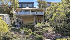 A modern two-story house with a balcony, surrounded by lush greenery and trees. - Wanda Point House - pure tranquillity and walk to beach (Salamander Bay)