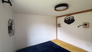 A room with a bed, a wall-mounted light fixture, a wall art piece, and a door handle.