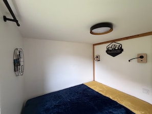 A room with a bed, a wall-mounted light fixture, a wall art piece, and a door handle.