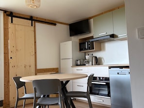 A compact kitchen with a wooden dining table, chairs, a microwave, a coffee maker, and a refrigerator. - Apartment in Les Menuires, 4 pers, ski-in/ski-out (Les Menuires)