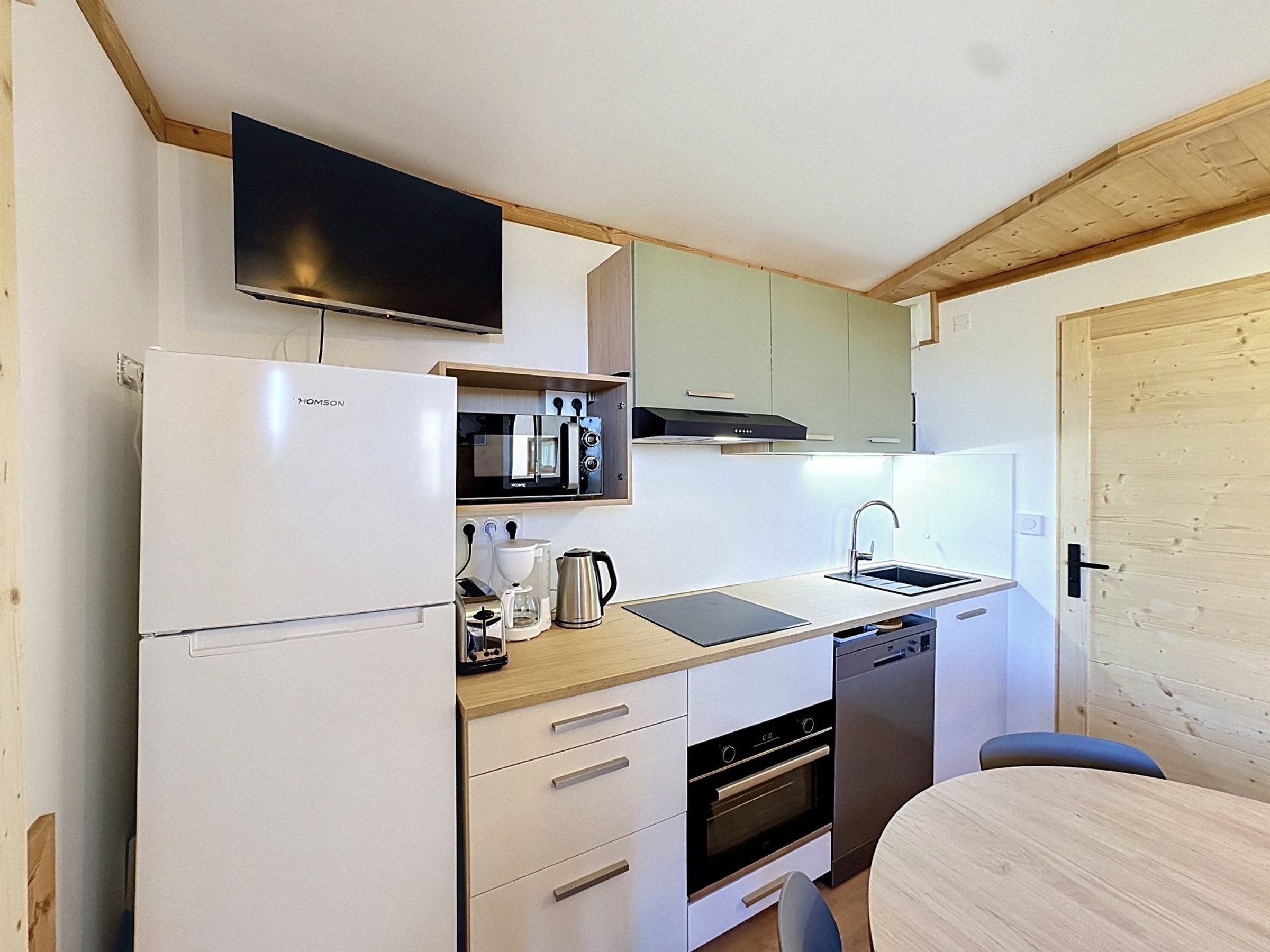 A compact kitchen with a built-in oven, a dishwasher, a microwave, and a flat-screen TV mounted above the counter.