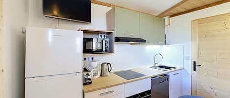 A compact kitchen with a built-in oven, a dishwasher, a microwave, and a flat-screen TV mounted above the counter.