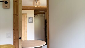 A wooden-framed doorway leading to a room with a round table and chairs, a wall-mounted light fixture, and a framed picture on the wall.