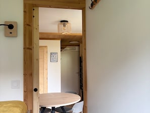 A wooden-framed doorway leading to a room with a round table and chairs, a wall-mounted light fixture, and a framed picture on the wall.