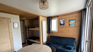 A room with a bunk bed, a sofa, a round table, and a window with curtains.