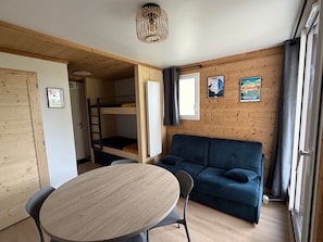 A room with a bunk bed, a sofa, a round table, and a window with curtains.