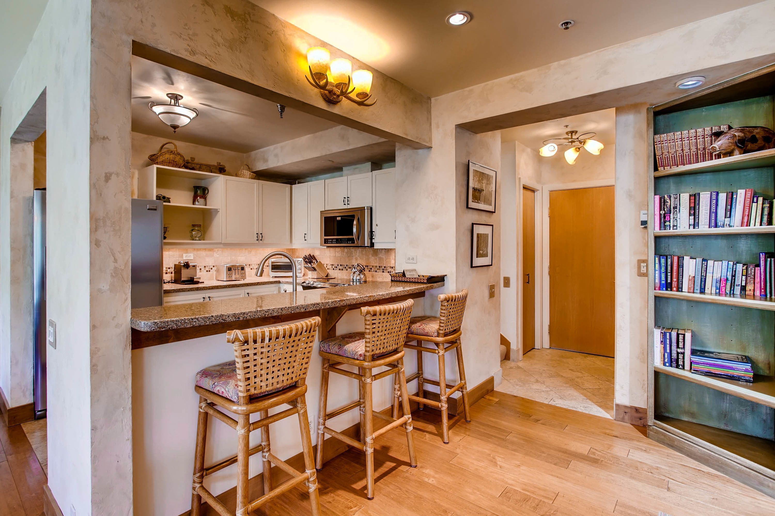 A kitchen with a central island, bar stools, a bookshelf, and a microwave.