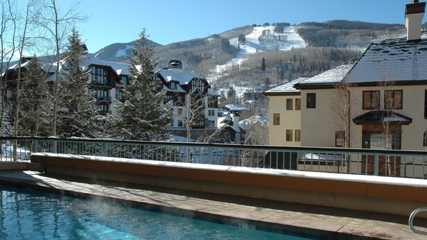 A pool area with a view of a mountain resort, including buildings and a ski slope. - Centennial 3 (Avon)