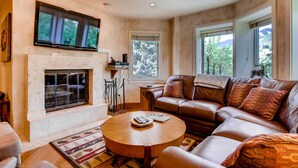 A living room with a fireplace, leather sofa, and a round coffee table. - Centennial 3 (Avon)