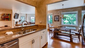 A modern kitchen with granite countertops, stainless steel appliances, and a dining area with a wooden table and chairs. - Centennial 3 (Avon)