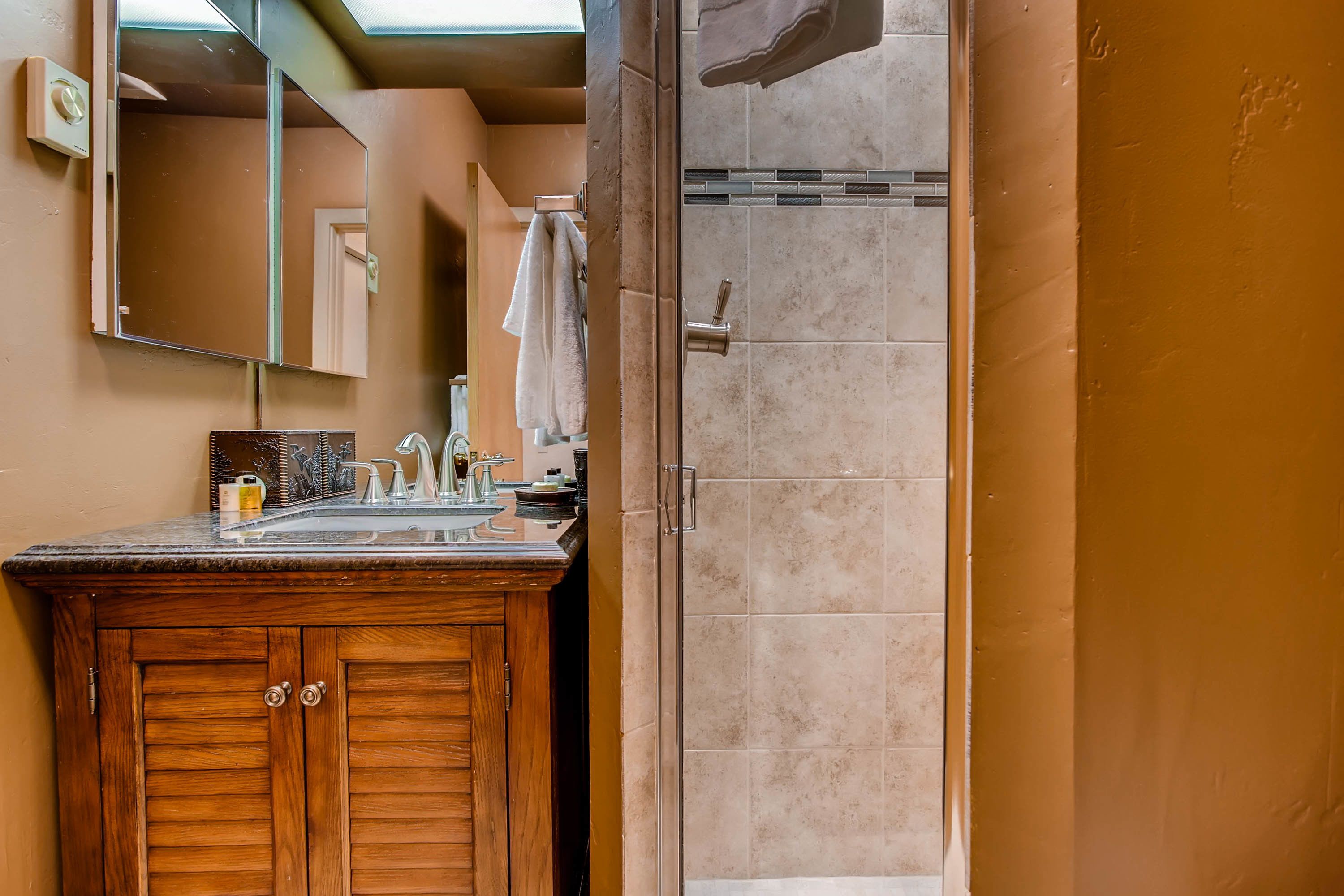 Une salle de bain avec un meuble-lavabo en bois, un lavabo avec un miroir et un espace douche.