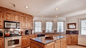 A kitchen with wooden cabinets, a stainless steel oven, a microwave, and a large island with a bowl. - Centennial 2 Bedroom Condo Unit no. 16 (Avon)
