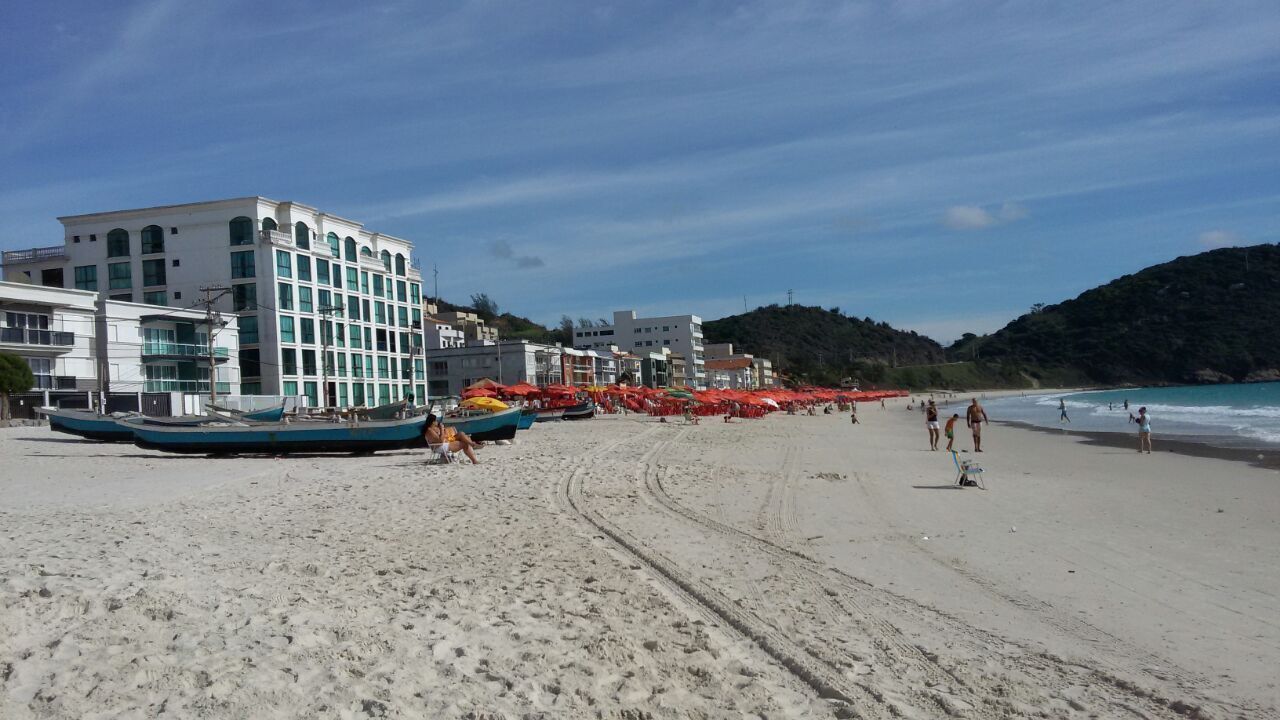 Een strand met boten, parasols en gebouwen op de achtergrond.