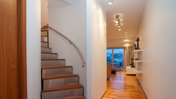 Ein modernes Interieur mit einer Holztreppe, einem Dielenbelag im Flur und einem Ausblick durch ein Fenster.