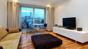 Ein modernes Wohnzimmer mit einer Couch, Hocker, Fernseher und einem Essbereich mit Tisch und Stühlen.
