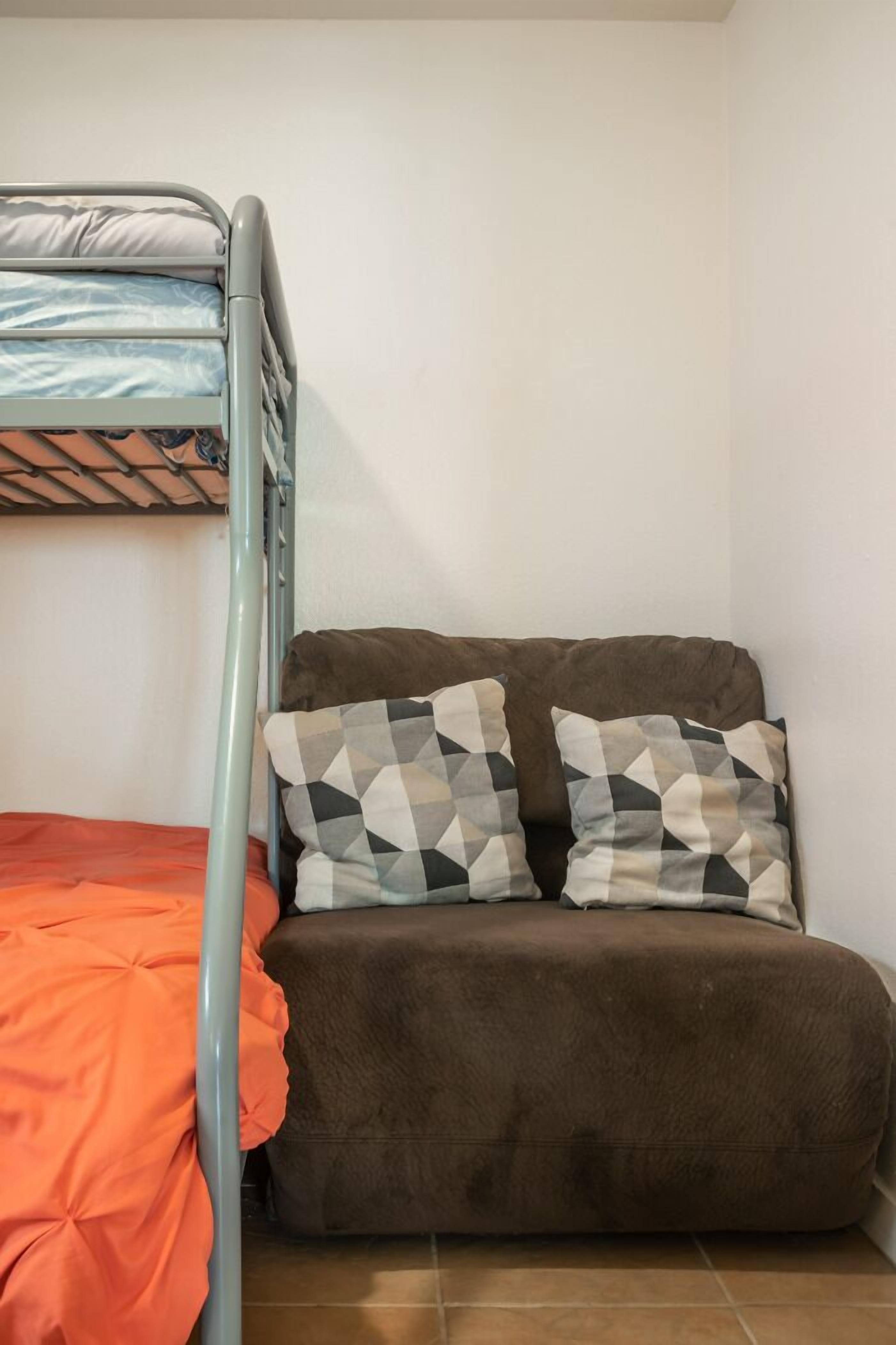 A bunk bed with a mattress and pillows, a sofa with a patterned cushion, and a red blanket.