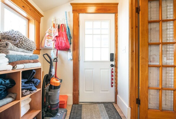Un couloir avec un aspirateur, des vêtements pliés rangés sur des étagères et une porte dotée d’un panneau en verre dépoli.