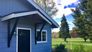 A blue building with a black door and windows, surrounded by a garden with plants and a lawn. - Racing Horse Ranch and Guest House with Golf (Grants Pass)