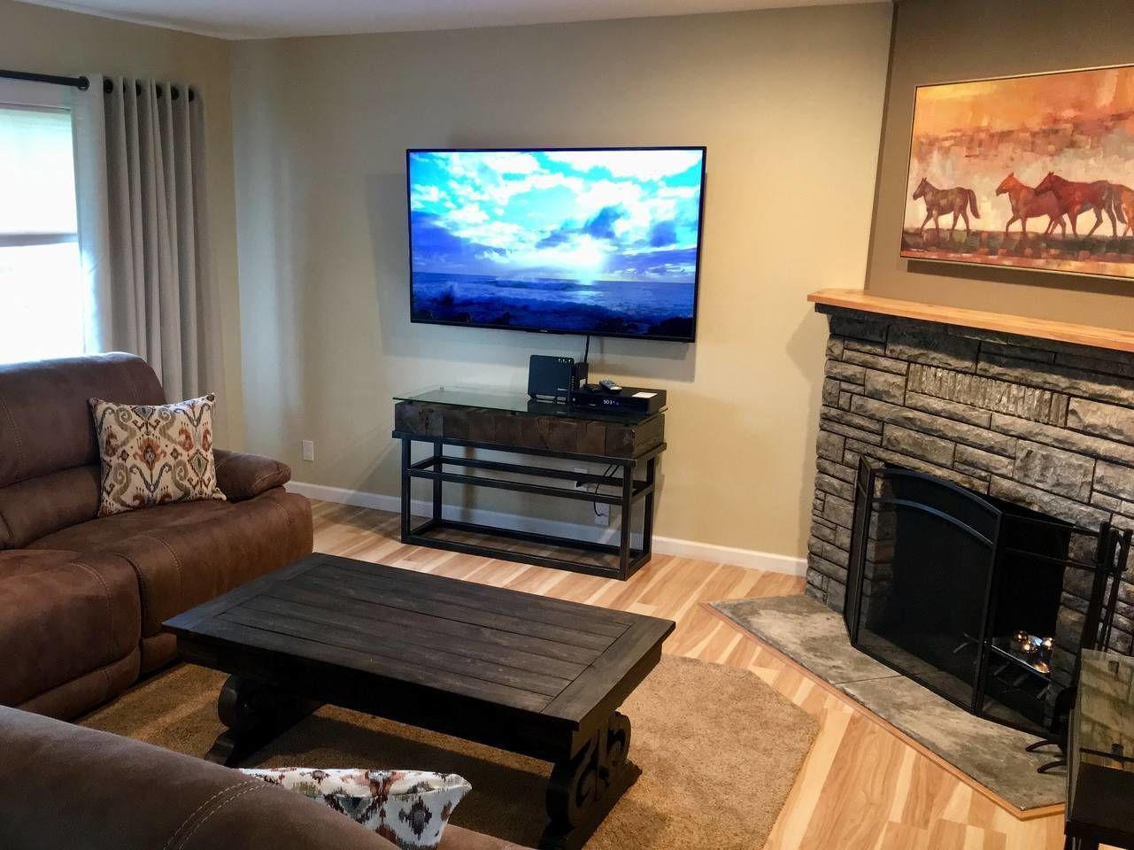 A living room with a leather sofa, a coffee table, a flat-screen TV, a glass table, and a stone fireplace.