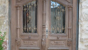Une porte en bois à deux battants, ornée de motifs en fer forgé, et un mur en pierre.
