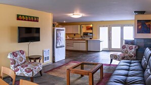 A living room with a sofa, chairs, a coffee table, a TV, and a kitchen in the background. - Hopyard View Farm - A Farm Experience in Ashland (Ashland)