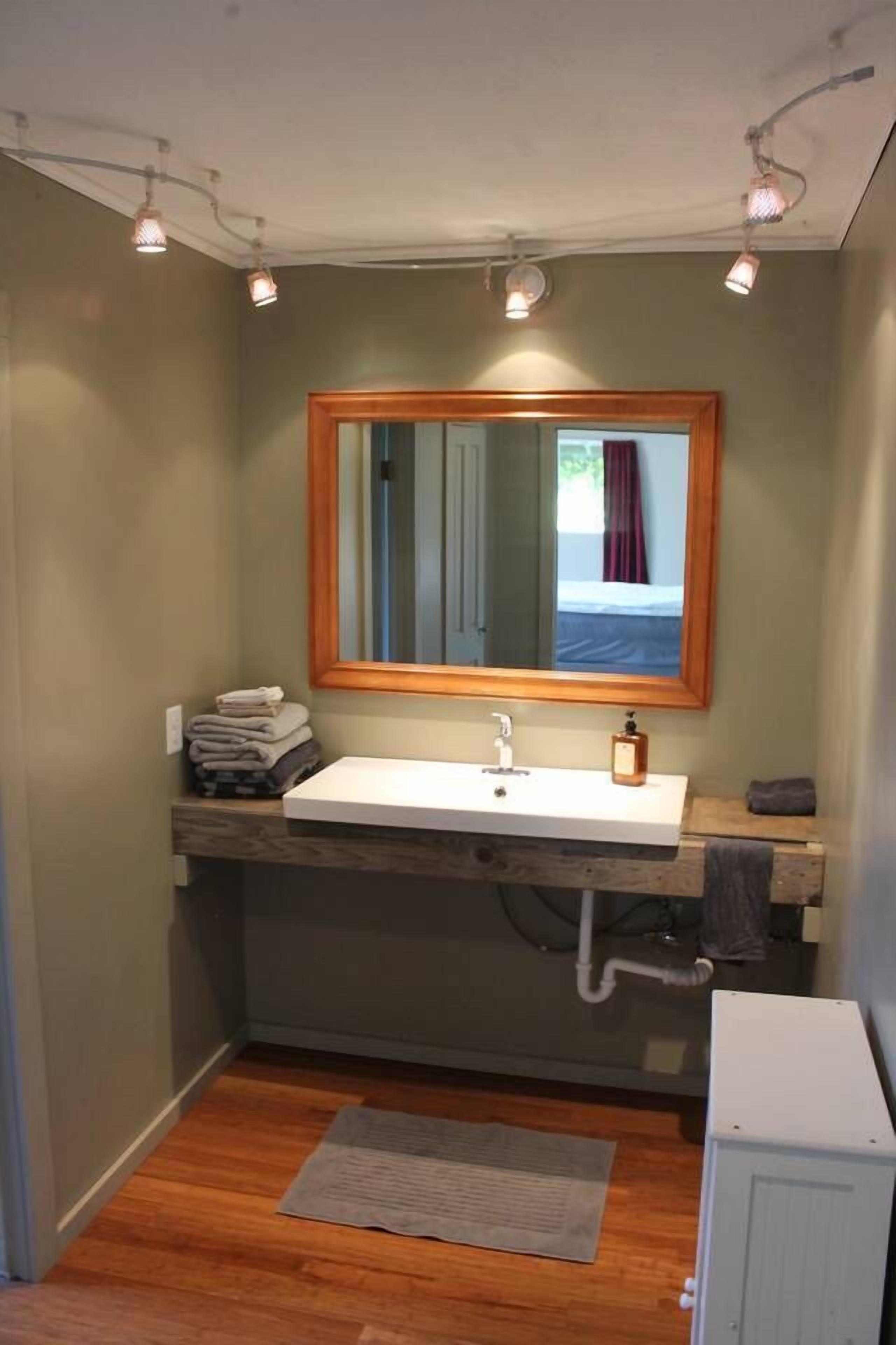 A small bathroom with a wooden vanity, a white sink, a mirror with a wooden frame, and a towel rack.