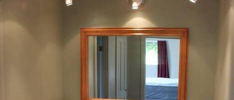 A small bathroom with a wooden vanity, a white sink, a mirror with a wooden frame, and a towel rack.