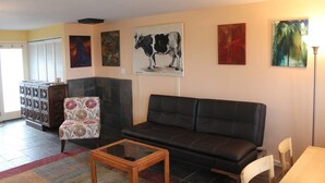 A living room with a black leather sofa, a patterned armchair, a glass coffee table, and a cabinet with decorative items. - Hopyard View Farm - A Farm Experience in Ashland (Ashland)