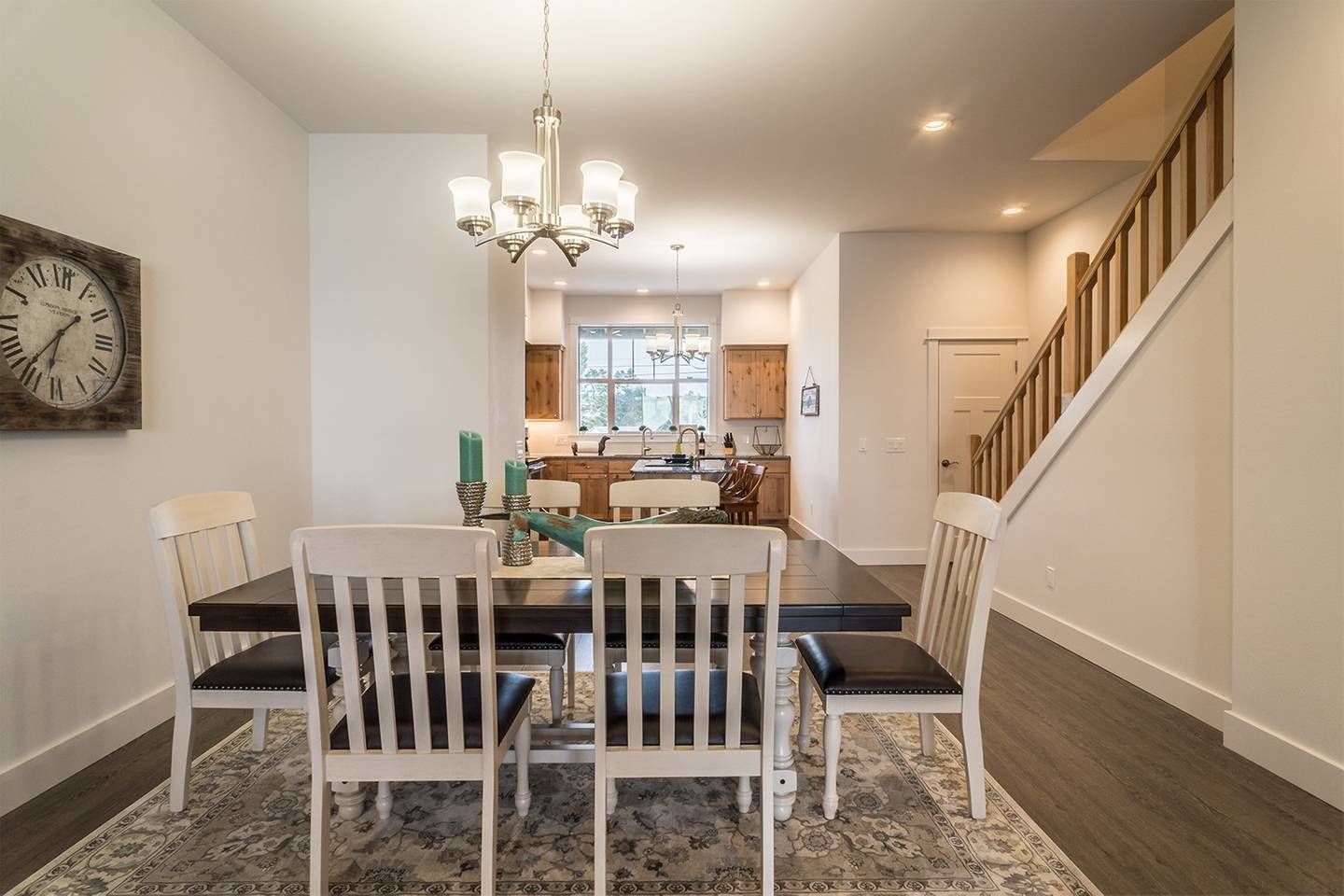 A dining area with a chandelier, a clock, and a staircase leading to another level.